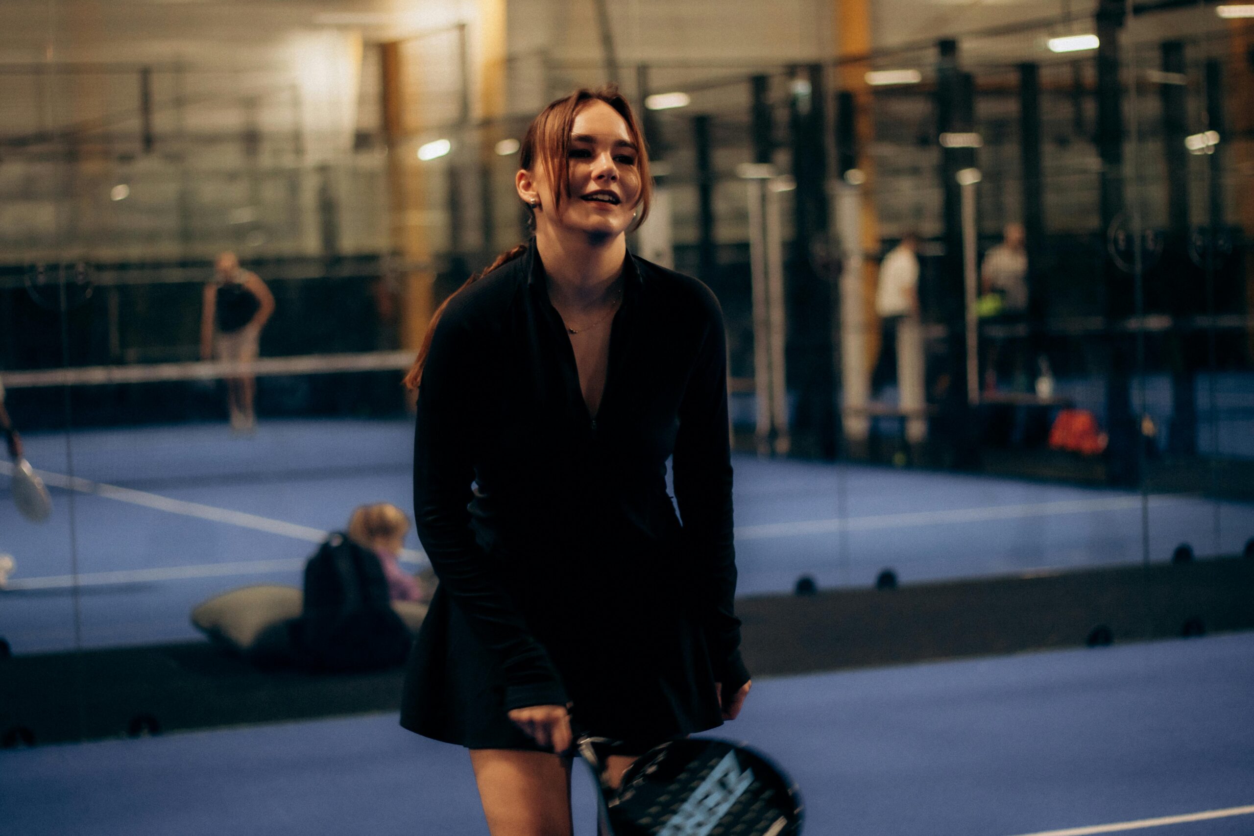 Woman smiling while holding a padel racket on an indoor padel court