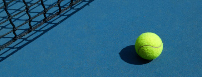 Yellow ball resting on a blue padel court next to the net